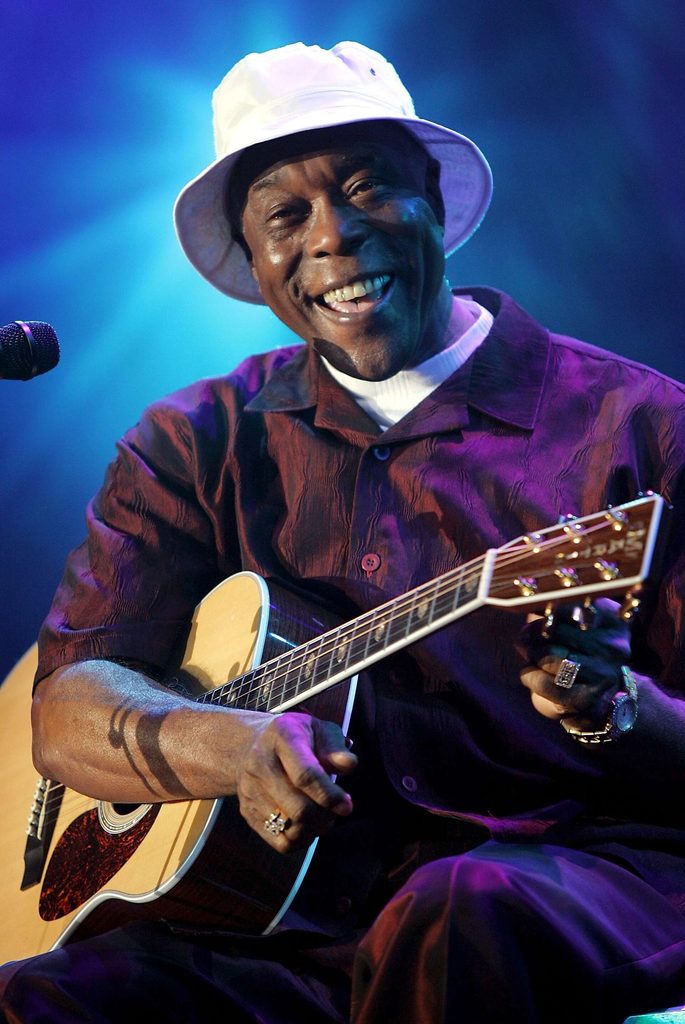 Buddy Guy, holding a guitar and smiling